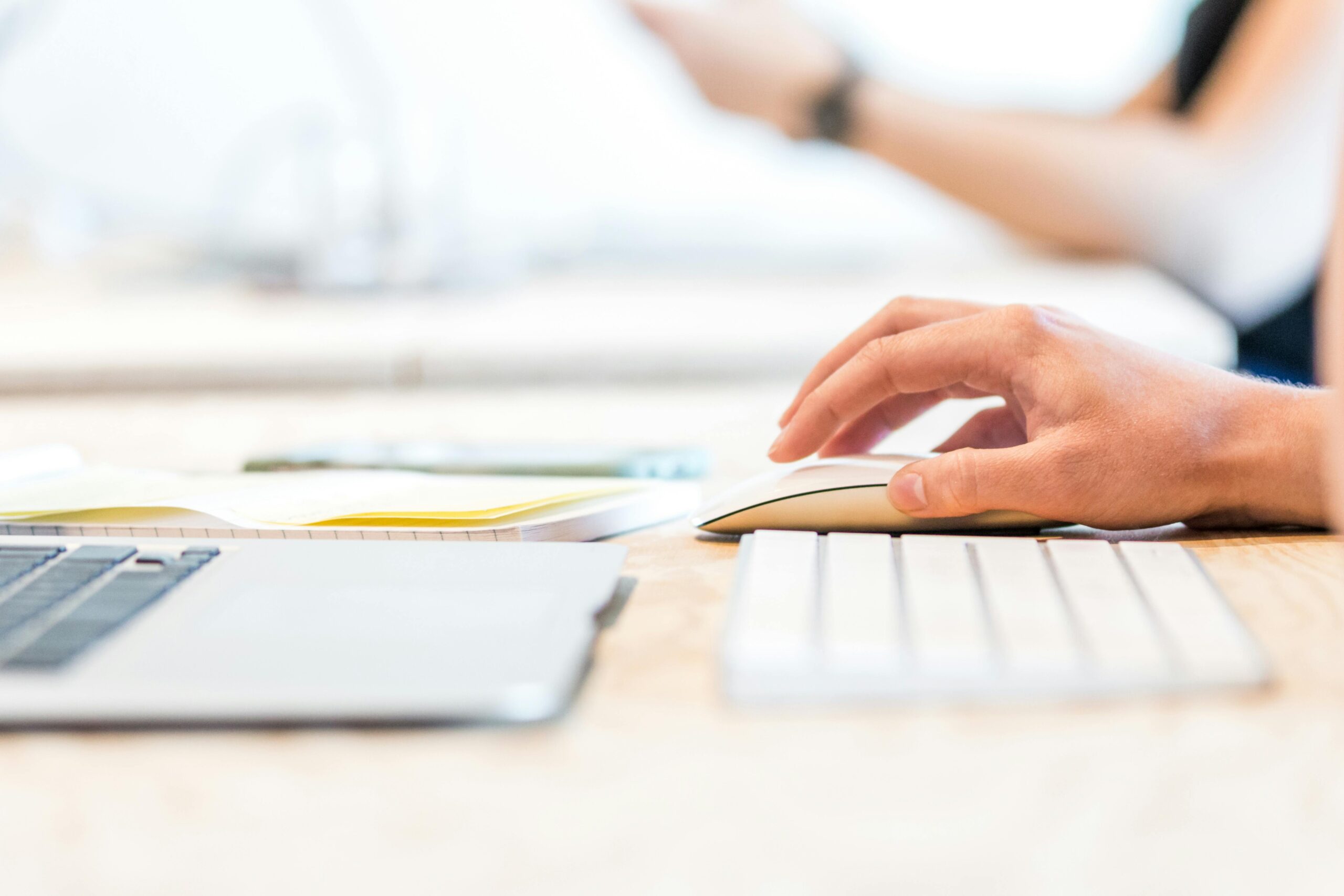 A person working at a laptop with a wireless mouse and keyboard in a bright office setting.